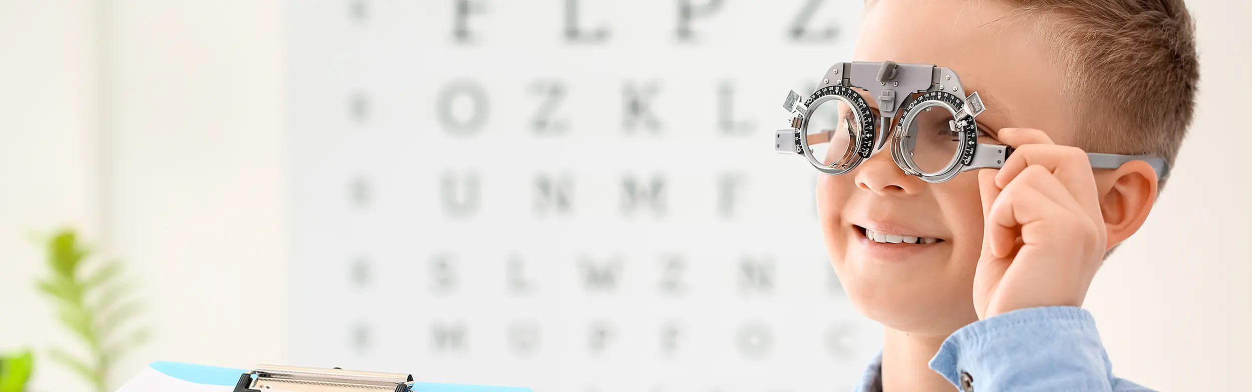 A young boy smiling as he places an eye examination in the shape of glasses on his eyes in an eye doctors office